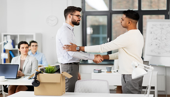 Employee shaking hands with a colleague while leaving a job, symbolizing an amicable exit.