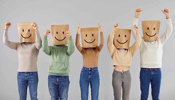 Group of people wearing paper bags with smiley faces, symbolizing anonymous feedback.