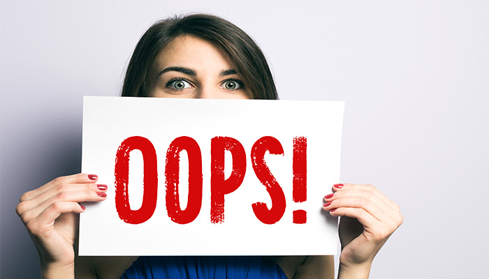 Woman holding a sign with 'Oops!' to emphasize the importance of compliance awareness.